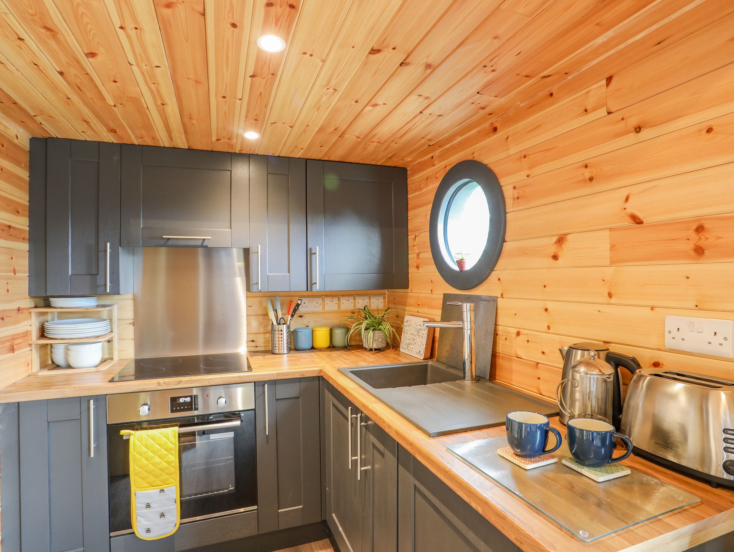 A modern kitchen with wooden walls, stainless steel appliances, and a round mirror.