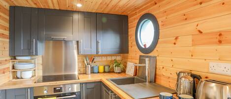 A modern kitchen with wooden walls, stainless steel appliances, and a round mirror.