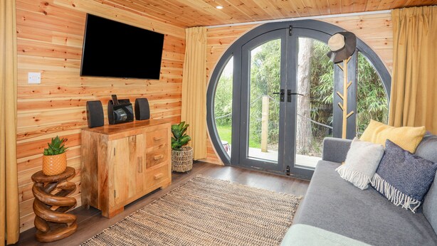 Ett mysigt rum med träpanel på väggarna, en platt-TV, en soffa och ett stort fönster med utsikt över grönområden.