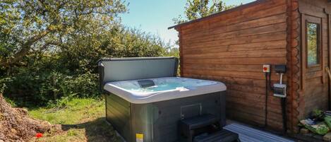 A wooden cabin with a hot tub and a small wooden deck.