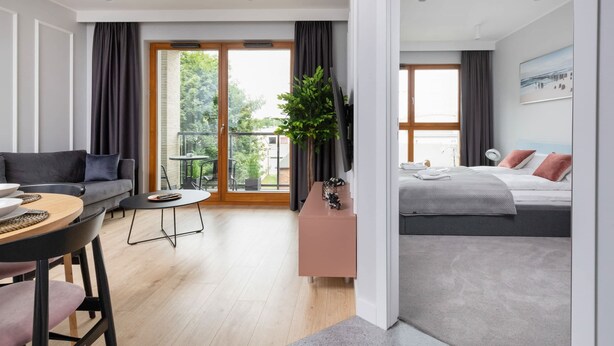 A modern hotel room with a sofa, a dining table, a small balcony, and a bed with a view of the outdoors. - Modern Apartment close to the Beach | Parking and Gym (Gdansk)