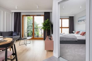 A modern hotel room with a sofa, a dining table, a small balcony, and a bed with a view of the outdoors. - Modern Apartment close to the Beach | Parking and Gym (Gdansk)