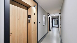 A modern hotel corridor with wooden doors, numbered room signs, and framed artwork on the walls. - Modern Apartment close to the Beach | Parking and Gym (Gdansk)