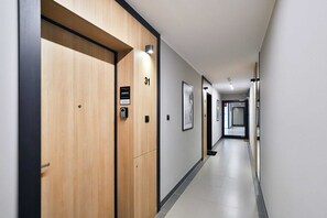 Un couloir d’hôtel moderne, avec des portes en bois, des panneaux indiquant le numéro des chambres et des œuvres d’art encadrées accrochées aux murs.