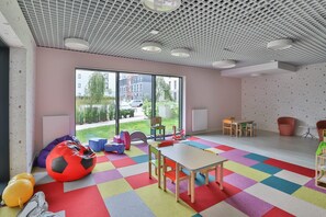 Une salle de jeux aux couleurs vives, dotée d’une grande fenêtre, d’une table, de chaises, de fauteuils en forme de poire et d’un sol coloré.