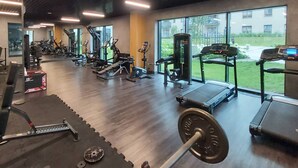 A gym with various exercise equipment, a treadmill, and a weight bench. - Modern Apartment close to the Beach | Parking and Gym (Gdansk)