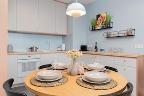 Une cuisine moderne aux murs bleu clair, aux armoires blanches et dotée d’une table à manger en bois, préparée pour accueillir quatre personnes.