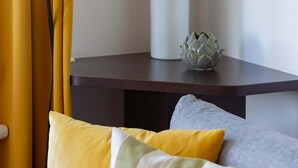 A corner of a room with a plant in a white vase, a small table with a decorative item, and a yellow curtain.