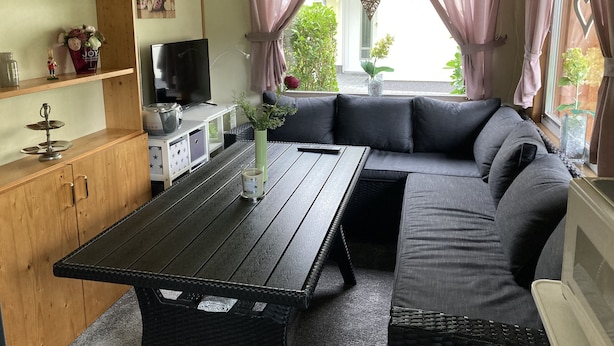 Un salon chaleureux avec une table en bois foncé, un canapé gris et un téléviseur posé sur un meuble blanc.