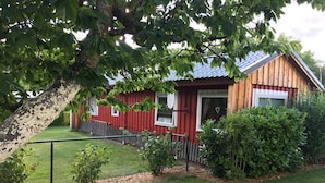 Une cabane en bois rouge, surmontée d’un toit en métal, entourée d’une pelouse bien entretenue et de divers arbustes.