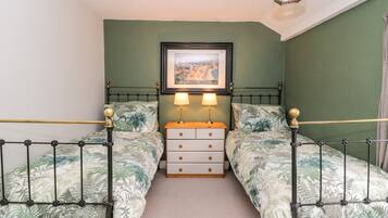 A bedroom with two beds, a nightstand, a framed picture, and a hanging light fixture.
