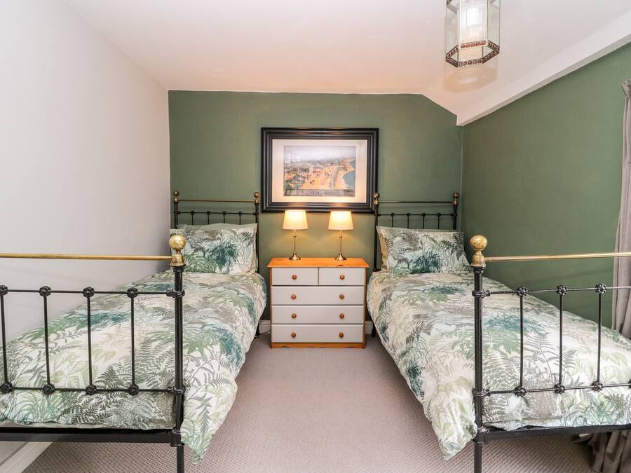 A bedroom with two beds, a nightstand, a framed picture, and a hanging light fixture.
