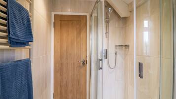 A modern bathroom with a glass shower enclosure, a wooden door, and a tiled floor.