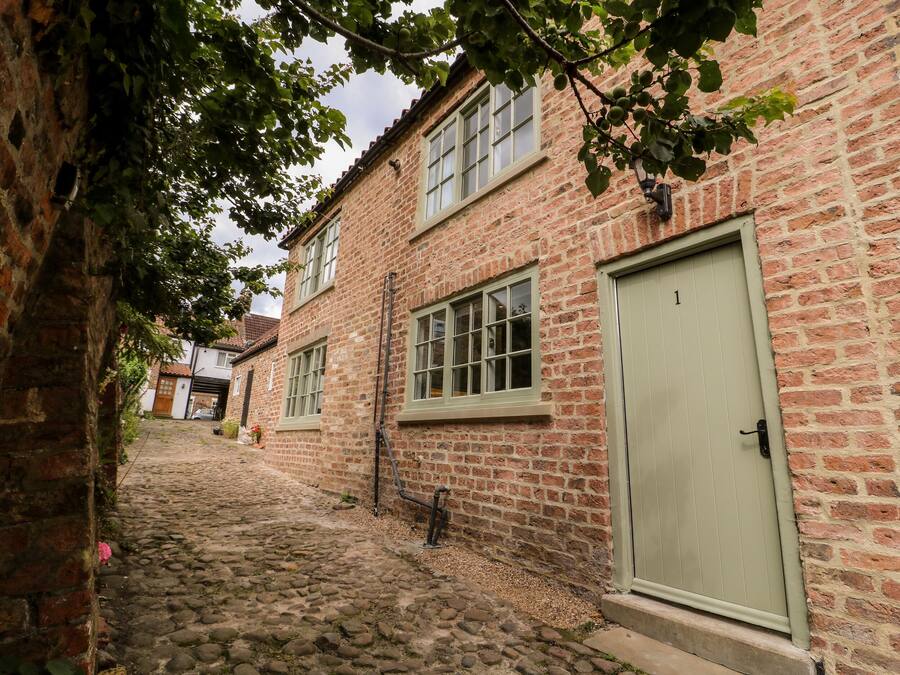 A narrow cobblestone street flanked by brick buildings with windows and a door.