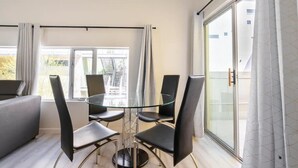 Een moderne kamer met een glazen tafel en vier stoelen, grote ramen en een balkon met uitzicht.