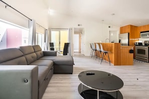 A modern living room with a grey sectional sofa, a round coffee table, and a dining area with a wooden island and chairs.