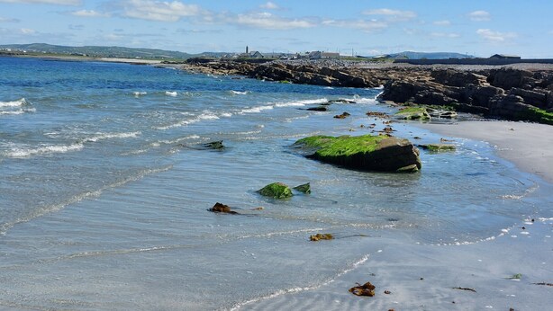 A beach with clear water, rocks, and a distant view of a town.