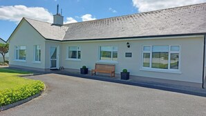 A single-story building with a grey tiled roof, white-framed windows, and a bench outside.
