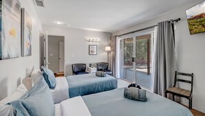 Habitación de hotel con dos camas, un escritorio, una silla y un amplio ventanal con cortinas.