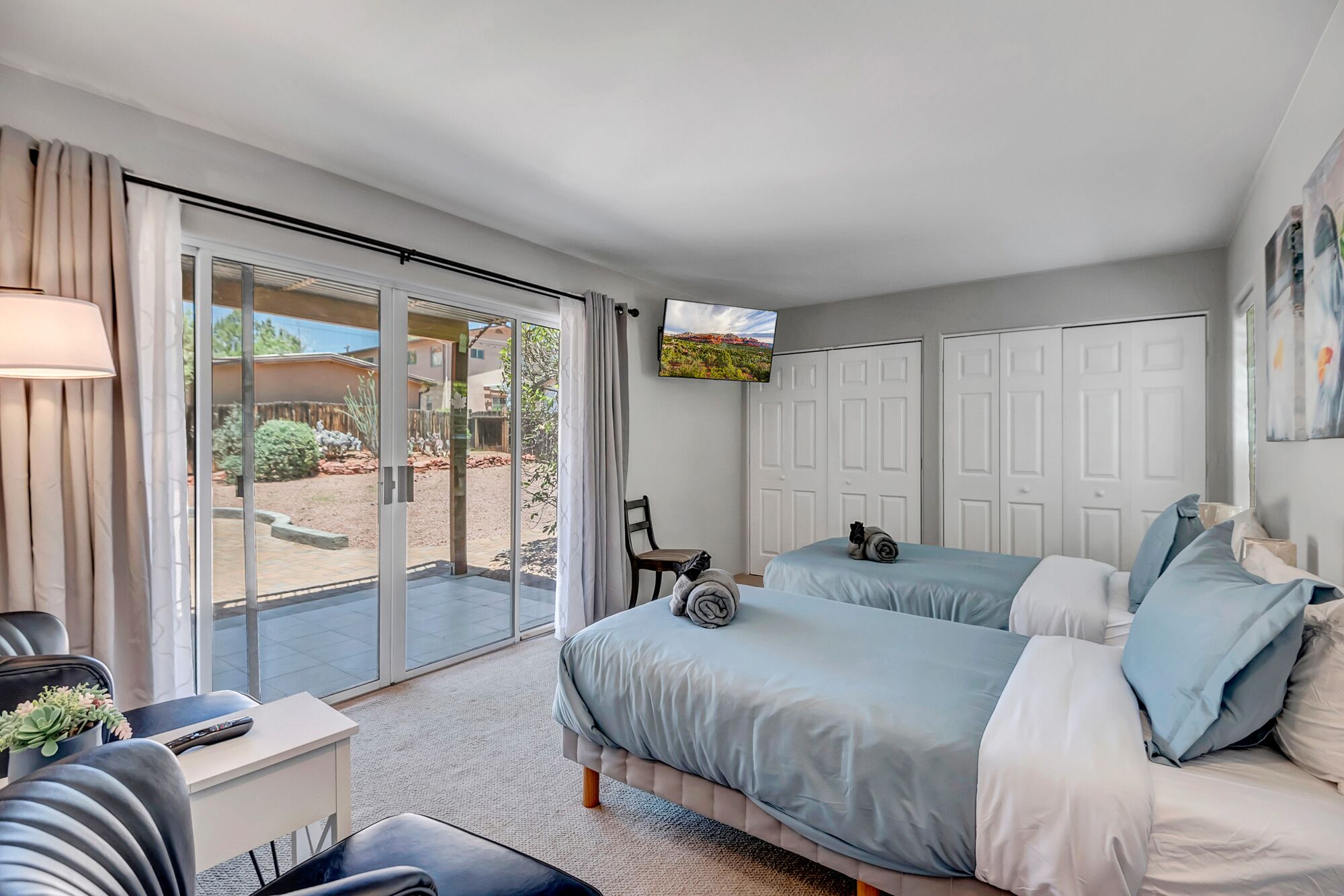 A bedroom with two beds, a TV, and a sliding glass door leading to an outdoor area.