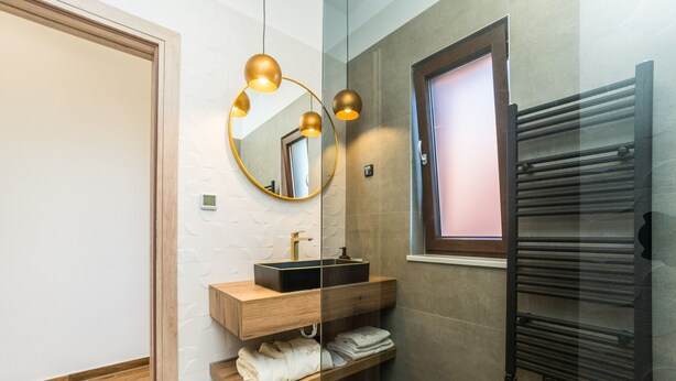 Une salle de bain moderne avec un meuble-lavabo en bois, un miroir rond, un porte-serviettes et une cabine de douche en verre.