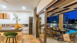 Una cocina moderna con una isla grande, un comedor con vista a la piscina y una puerta de vidrio que da a un espacio exterior.