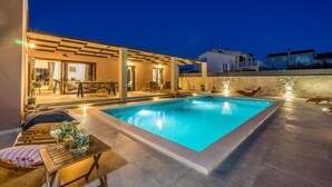 Une piscine avec une terrasse carrelée, un espace extérieur aménagé avec des sièges et un coin abrité comprenant une table et des chaises.