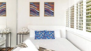 A modern bedroom with a large bed, a patterned pillow, and two abstract paintings on the wall. - Getawayz NSW - Bay Court III -Spacious Waterside Studio next to Hayes Beach, Cafes & Ferry! (Neutral Bay)