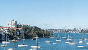Un puerto deportivo con varios veleros amarrados, un horizonte urbano al fondo y edificios con techos de tejas rojas.