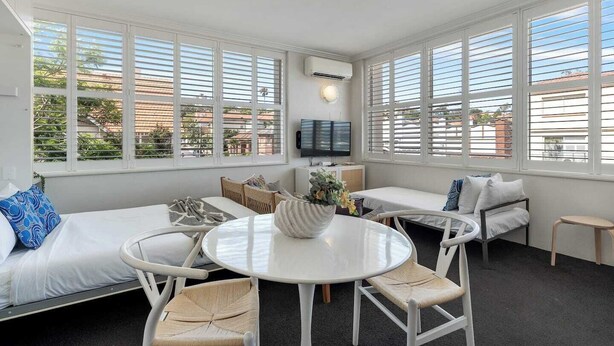 Una habitación moderna, bien iluminada, con ventanas amplias, una mesa redonda y zonas de estar cómodas.