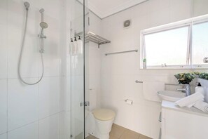 Une salle de bain moderne avec une douche à parois de verre, des toilettes, un lavabo avec une fenêtre au-dessus et un porte-serviettes.