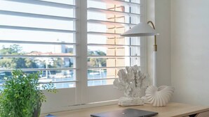 Escritorio con una laptop, una lámpara blanca y corales decorativos junto a una ventana con persianas.