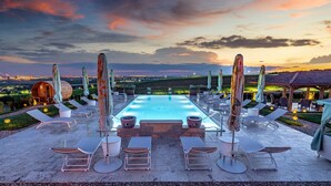 A pool area with lounge chairs and umbrellas, a wooden barrel, and a view of the landscape.