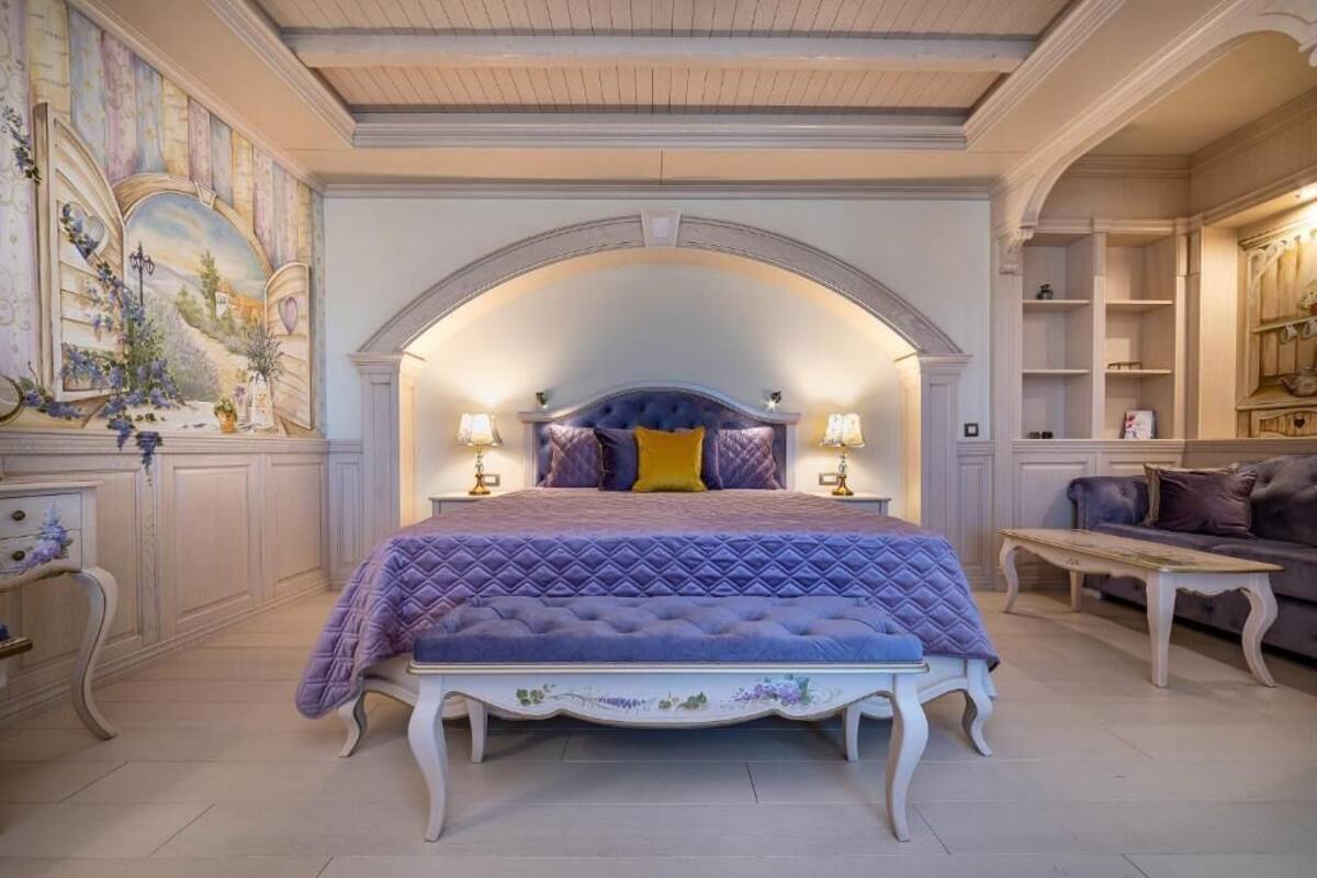 A bedroom with a large bed, two bedside lamps, and a decorative arched ceiling.