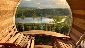 A circular wooden structure with a bench inside, offering a view of a lake and surrounding landscape.