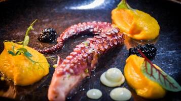 A dish with octopus, mango, and blackberries on a dark plate.