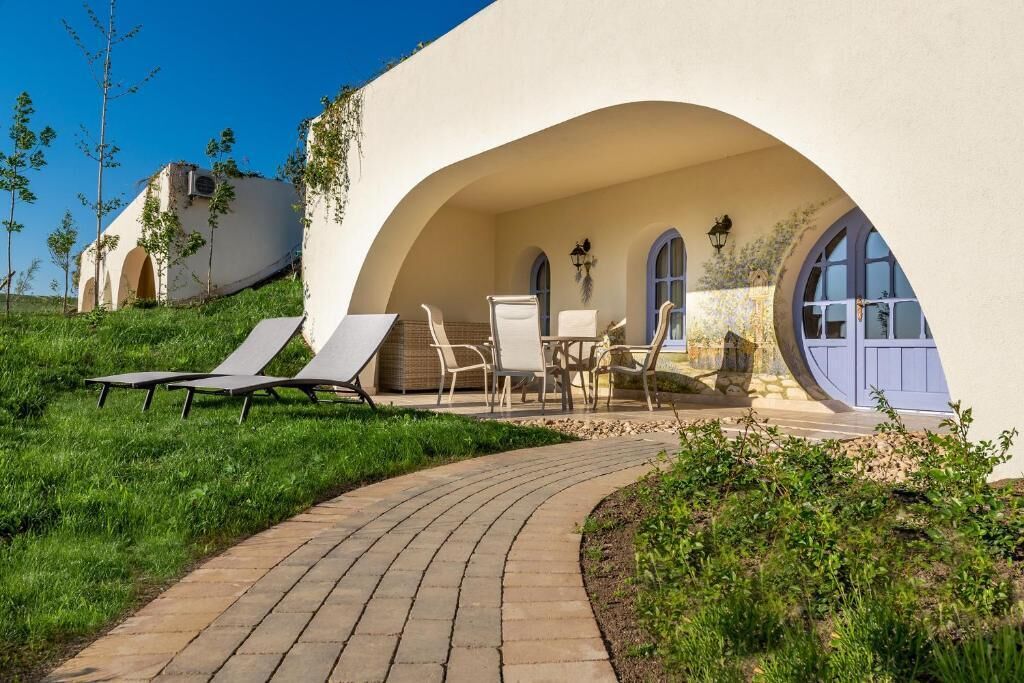 Uma villa moderna com um arco curvo que dá para uma área de pátio com espreguiçadeiras e uma mesa.