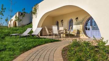 Uma villa moderna com um arco curvo que dá para uma área de pátio com espreguiçadeiras e uma mesa.