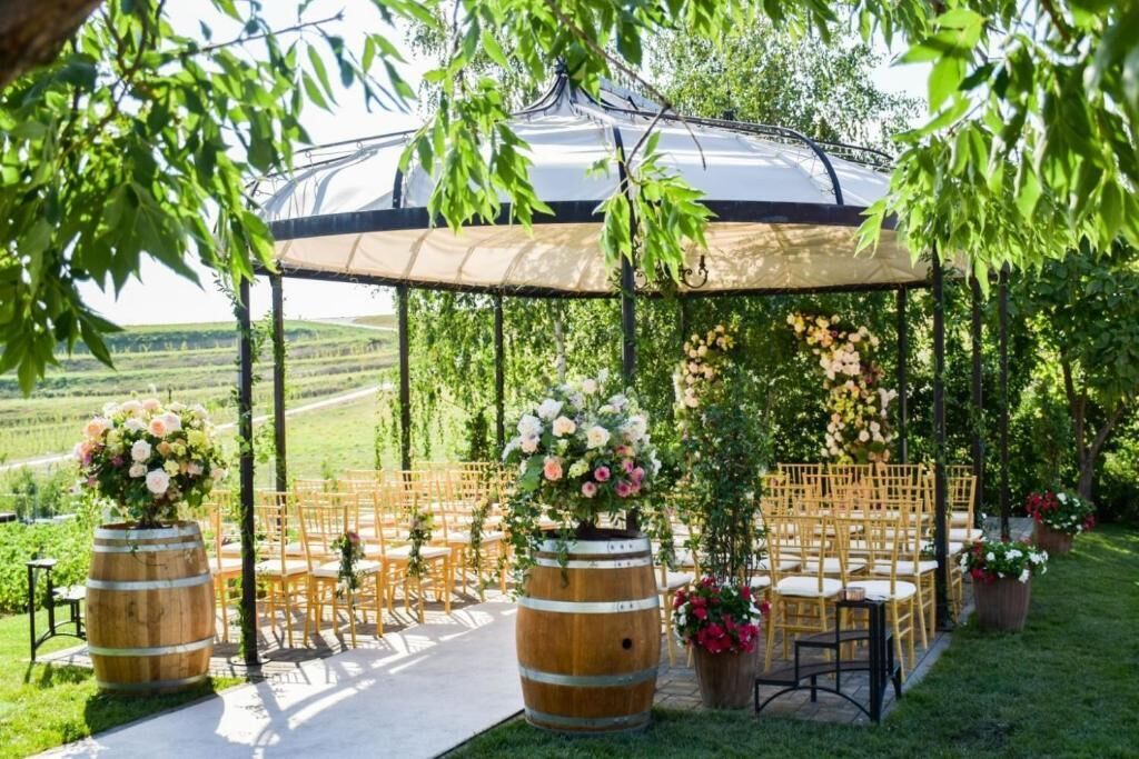 An outdoor wedding venue with a covered seating area, wooden chairs, and floral arrangements.