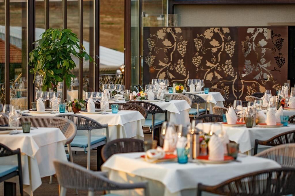 An outdoor dining area with tables set for multiple guests, featuring white tablecloths and wicker chairs.