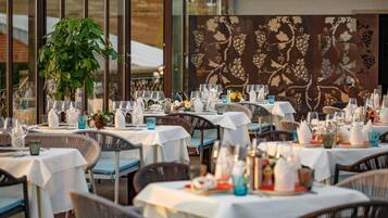 An outdoor dining area with tables set for multiple guests, featuring white tablecloths and wicker chairs.