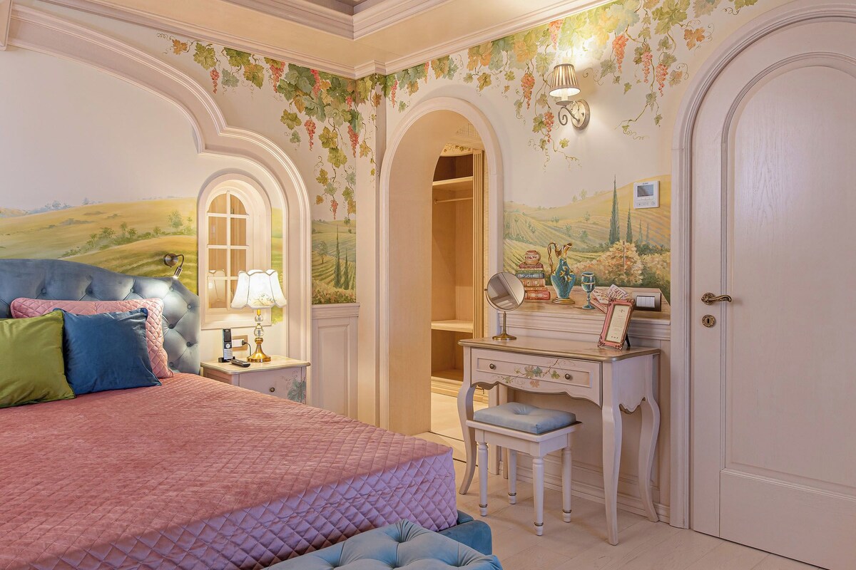 A bedroom with a bed, a vanity with a mirror, and a dresser.