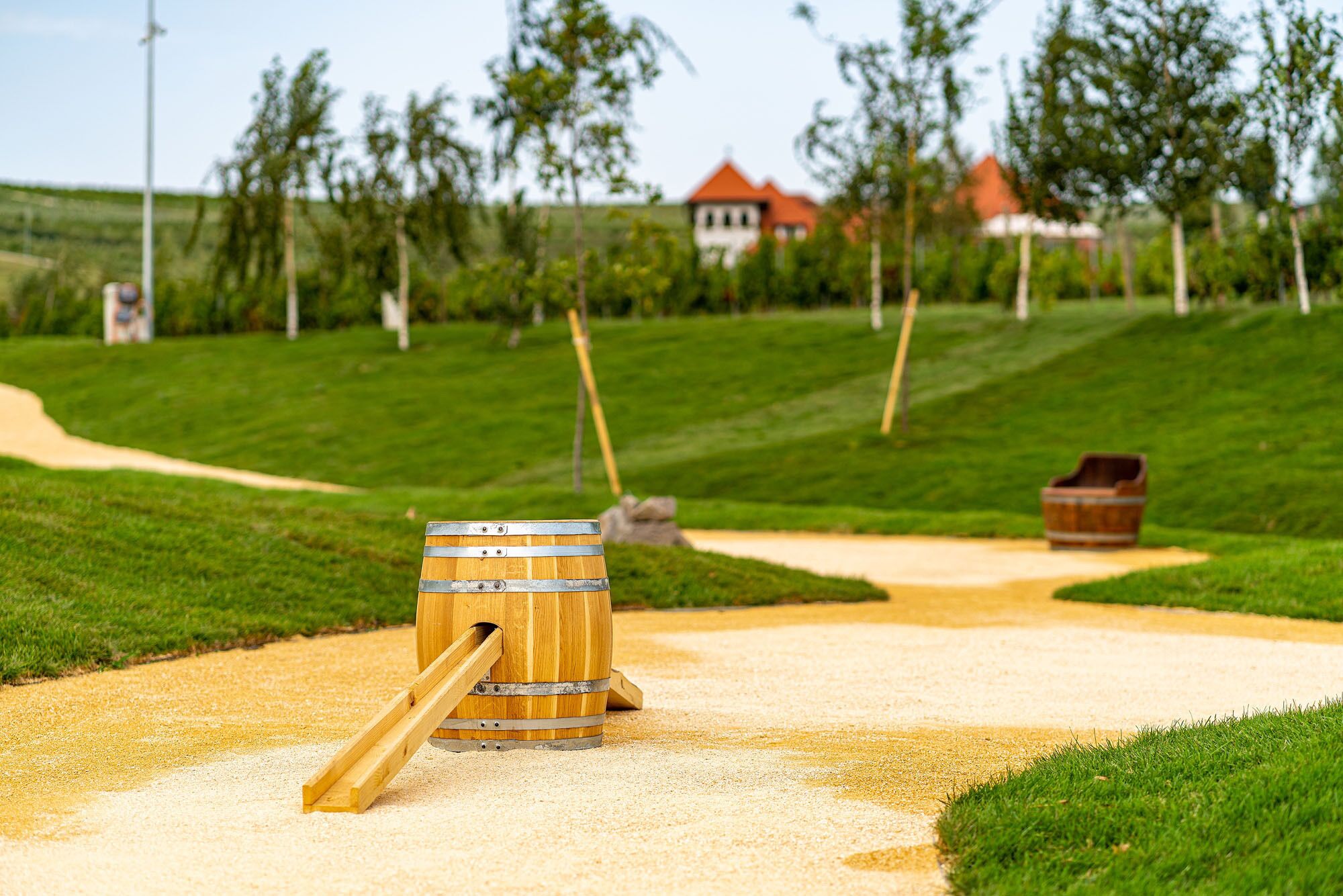 A wooden barrel with a lever on a gravel path in a park with grass and trees.