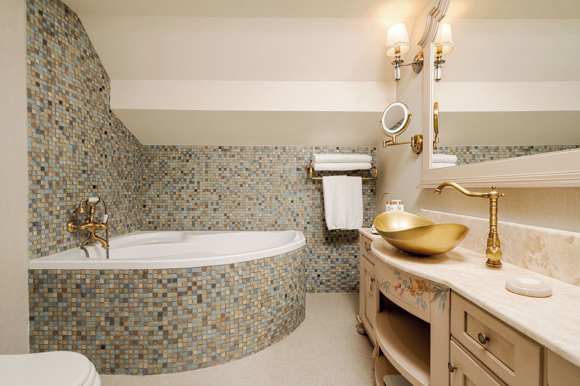 A bathroom with a mosaic tile wall, a freestanding bathtub, a gold basin, and a vanity with a mirror.