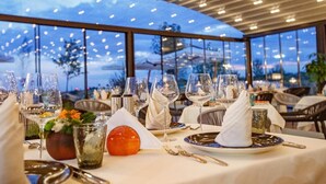 A restaurant setting with tables set for dining, featuring a view through large windows and a modern ceiling design.