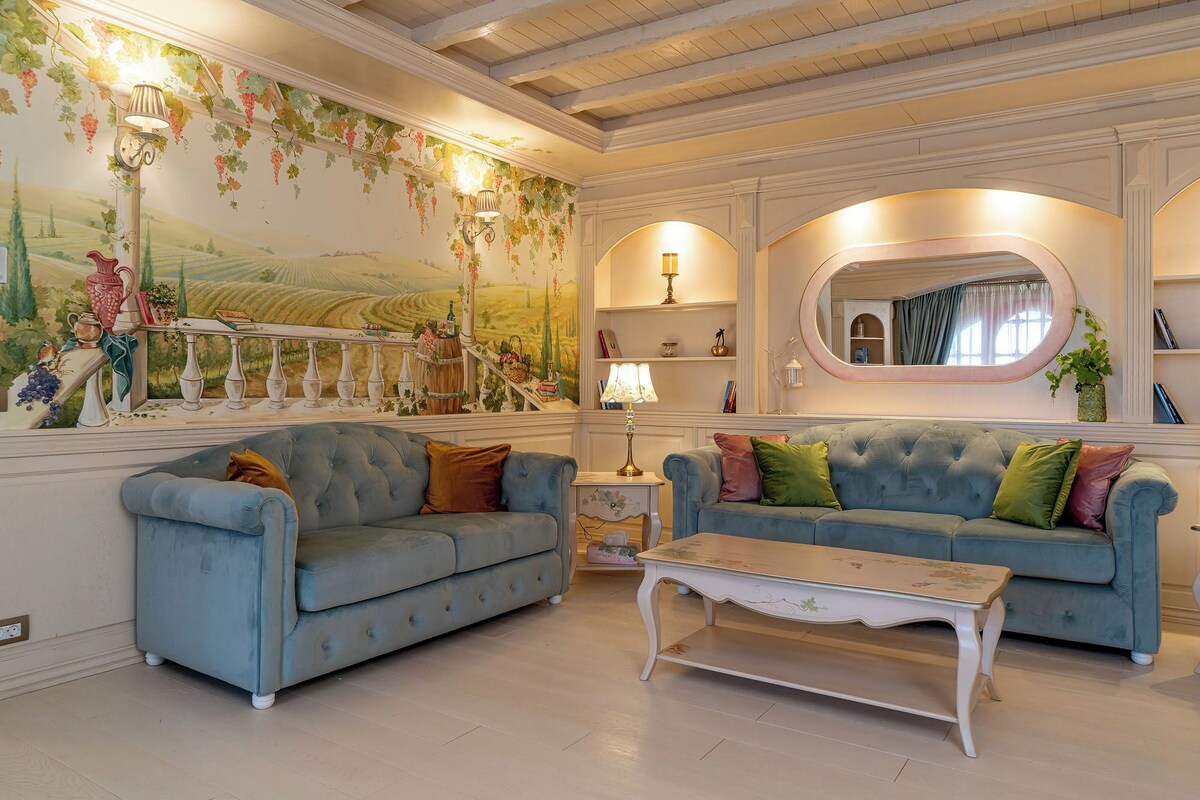 A living room with two blue sofas, a white coffee table, and a mural of vineyards on the wall.