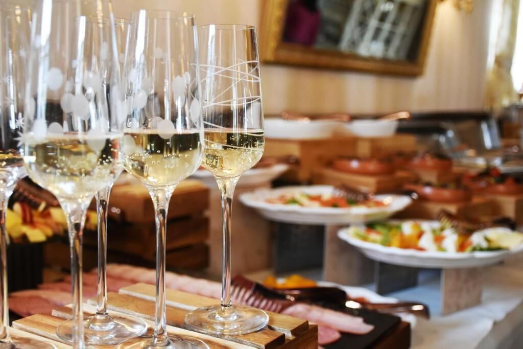 Un espace repas avec de nombreux verres à vin disposés sur une table en bois, entourée de différents plats et d’un buffet.