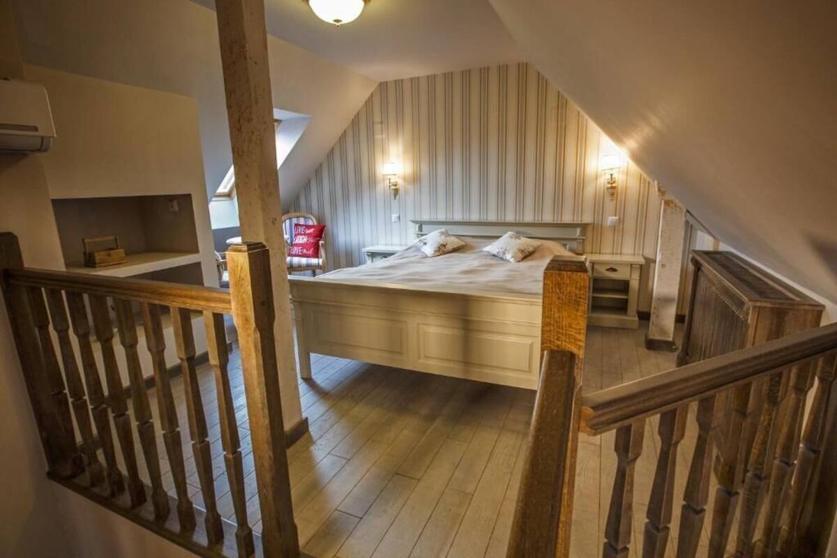 A bedroom with a sloped ceiling, a bed, a nightstand, a lamp, and a view of the kitchen.