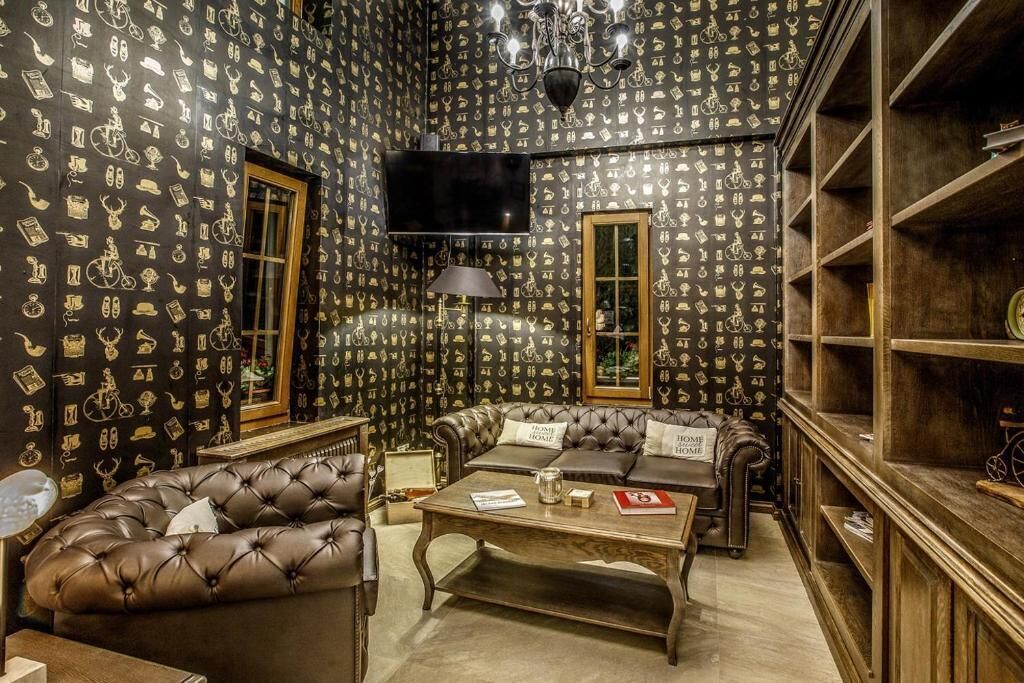 Una habitación con papel tapiz estampado, televisión, sofá, mesa de centro y estantería.