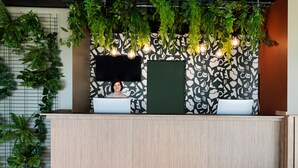 Un mostrador de recepción de diseño moderno, con un muro con motivos, plantas colgantes y un televisor de pantalla plana.